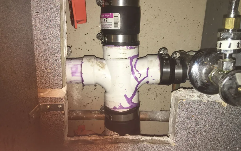 A PVC drain fitting and supply valves opened up in a block wall during a commercial plumbing repair
