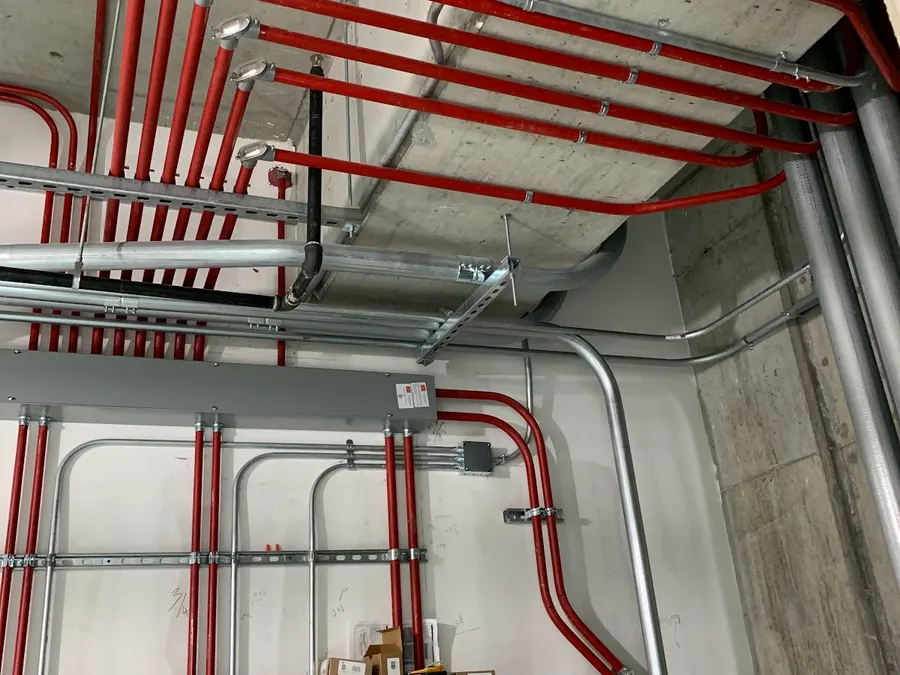 Red and silver conduit runs along a concrete wall and ceiling in a commercial building