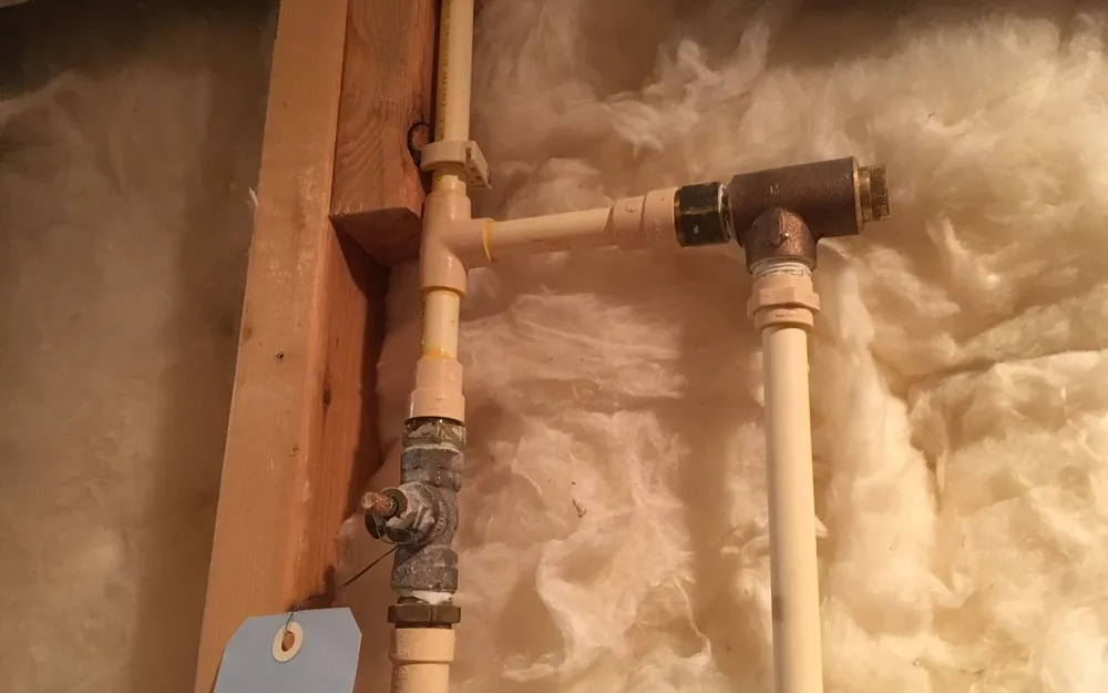 A water supply line with a shutoff valve inside an insulated stud wall during a home plumbing repair