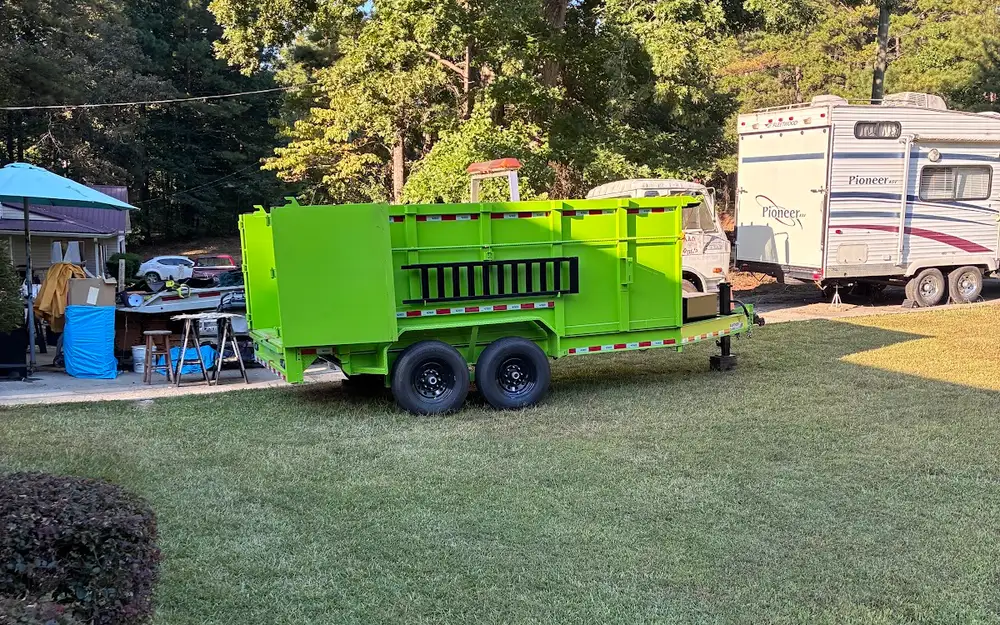 A green rubber tire dump trailer parked on a mowed lawn for a cleanout job